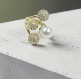 Anillo abierto dorado de diseño contemporáneo con tres balines cubiertos de microcircones brillantes y una perla blanca esférica.