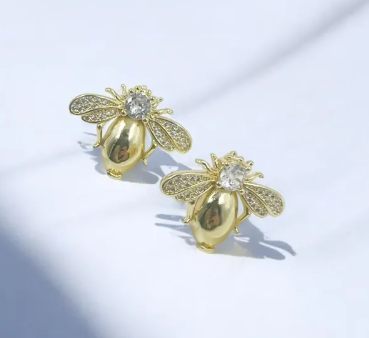 Aretes dorados pequeños tipo topo con silueta de mosquita decorada con microcircones brillantes.