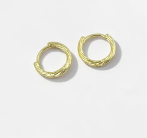 Aretes tipo candonga dorada con bisel ondulado y líneas fluidas de acabado liso y brillante.