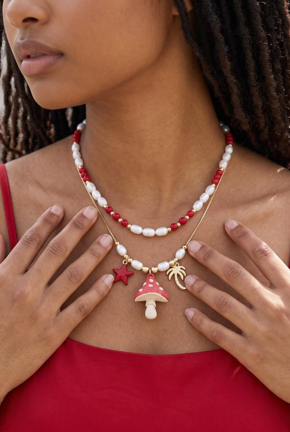 Set de dos collares en tonos rojo, blanco y dorado con dije de hongo y detalles inspirados en la naturaleza tropical.