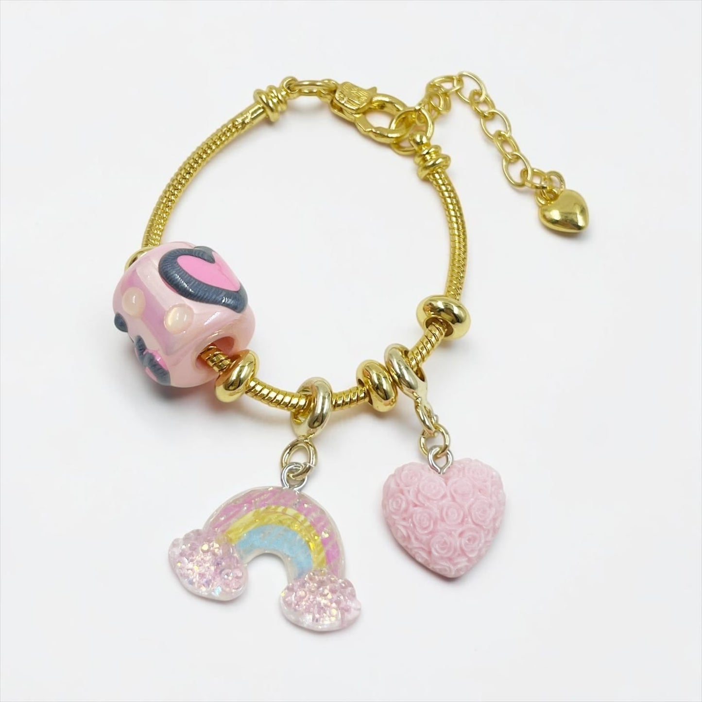 Pulsera de guaya dorada con dijes de resina y detalle de arcoíris que brilla en la oscuridad