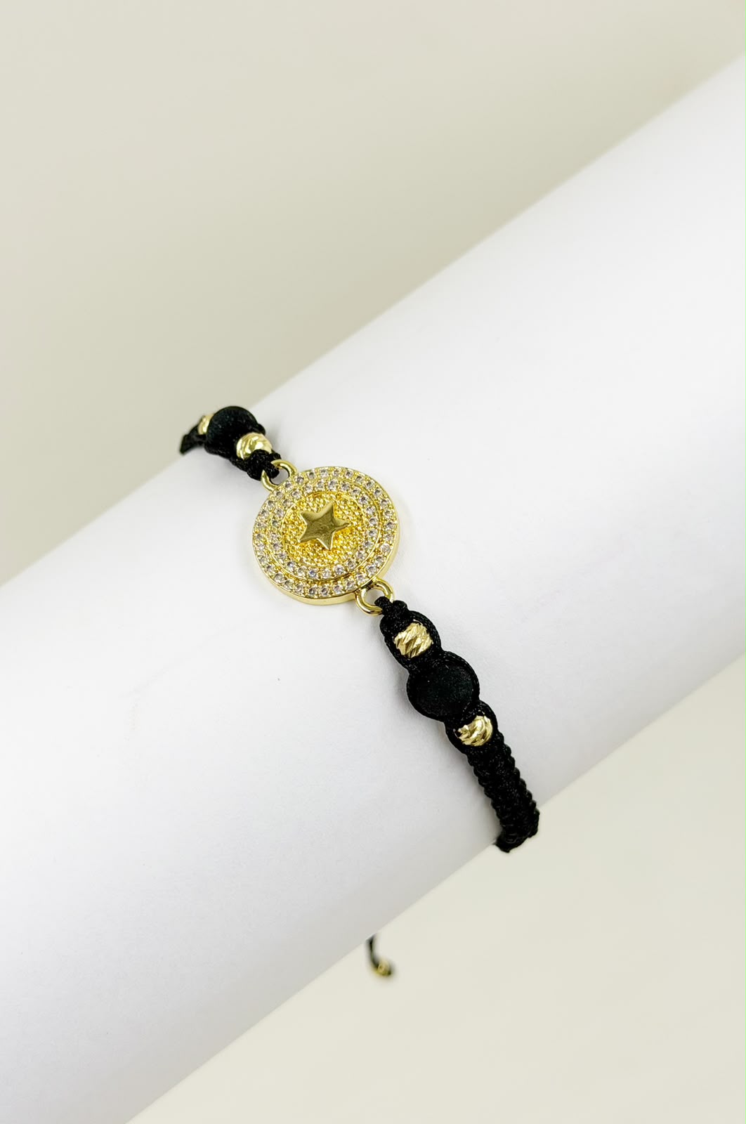 Pulsera artesanal con dije de medalla y estrella grabada, decorada con detalles brillantes.
