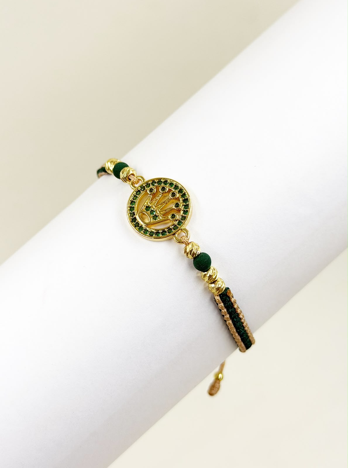 Pulsera artesanal con dije de medalla, corona grabada y detalles brillantes.
