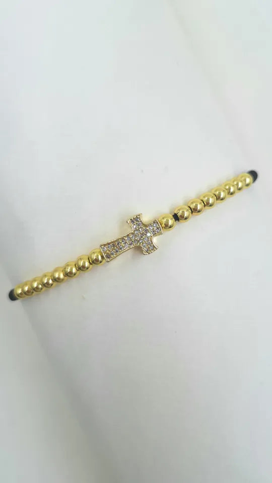 Pulsera Cruz Destellos en macramé con balines dorados y dije cruz rodinada con microcircones