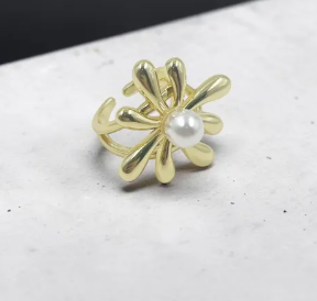 Anillo ajustable dorado con diseño de flor de pétalos lisos y redondeados, con una perla blanca en el centro sobre fondo claro.