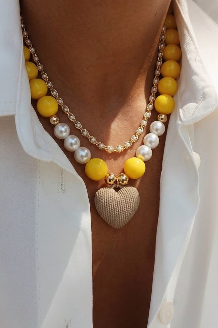Set de dos collares con diseño en capas, cuentas en tonos amarillo y perla, y dije de corazón con relieve 3D.