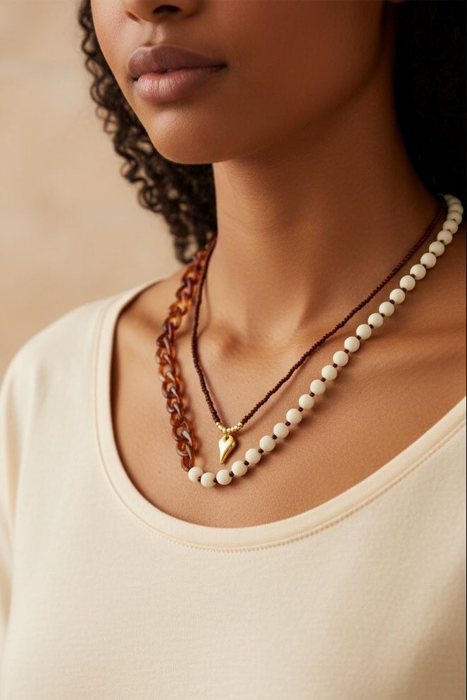 Collar de diseño dinámico con cuentas, eslabones y dije decorativo.