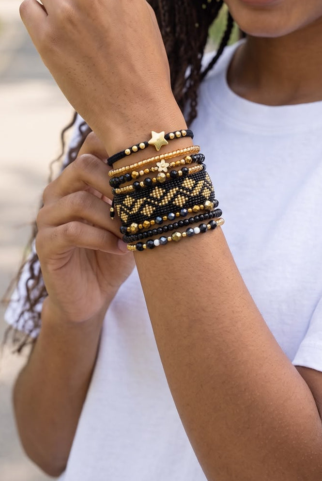 Maxipulsera de 8 vueltas con tejido central de fondo negro y rombos dorados, acompañada de cuentas y detalles decorativos.