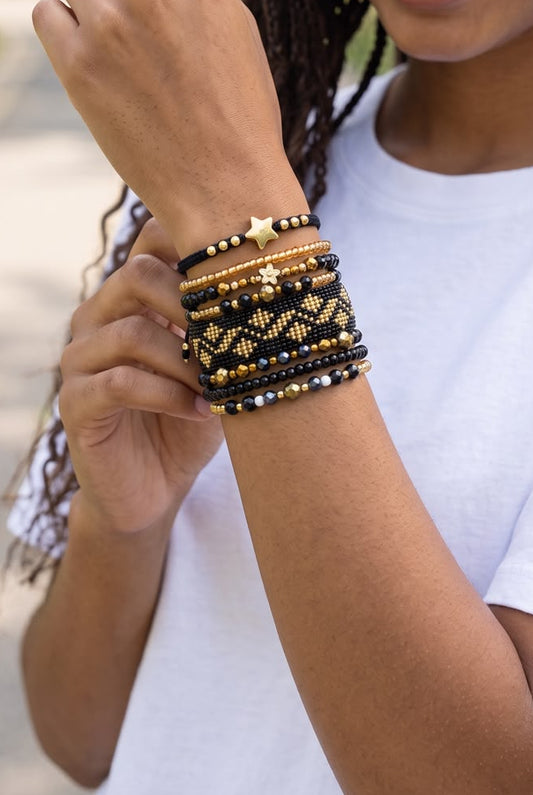 Maxipulsera de 8 vueltas con tejido central de fondo negro y rombos dorados, acompañada de cuentas y detalles decorativos.