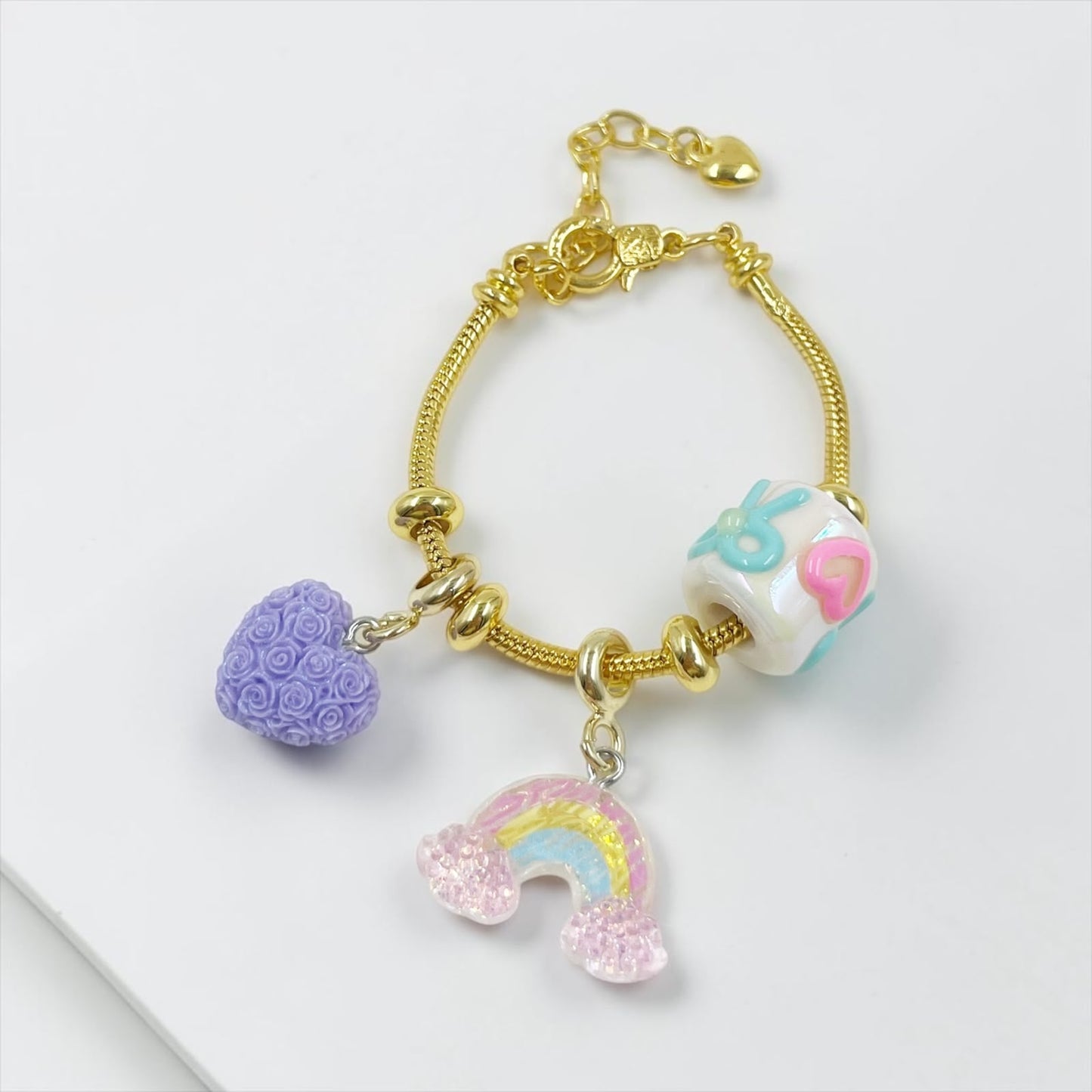 Pulsera de guaya dorada con dijes de resina y detalle de arcoíris que brilla en la oscuridad