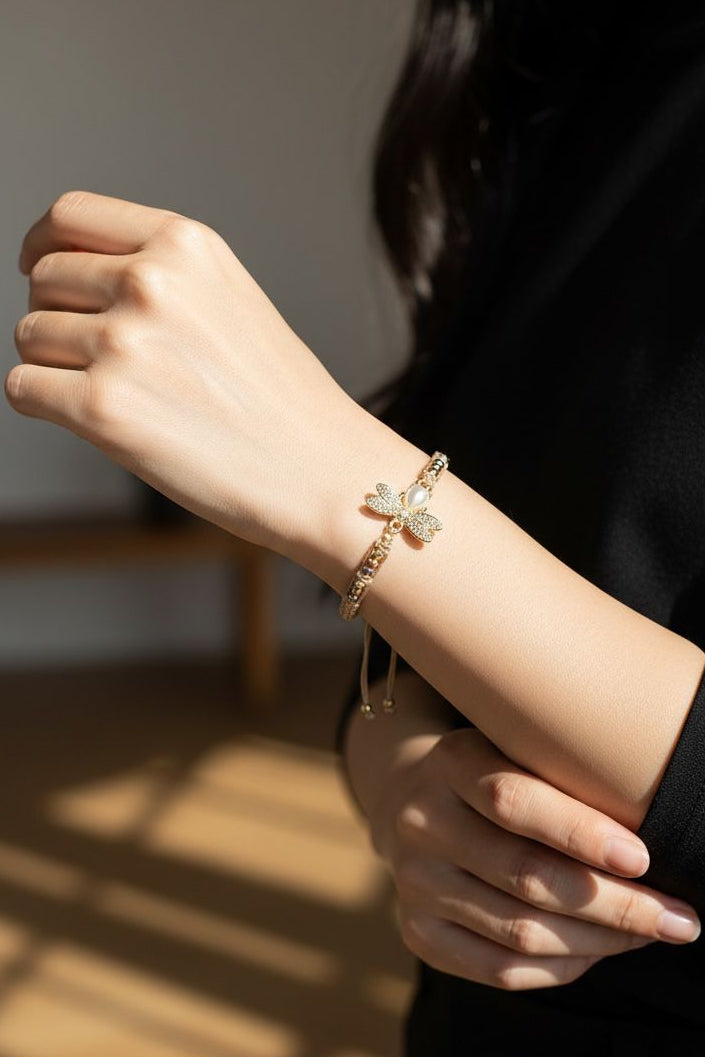 Pulsera artesanal de macramé con dije de libélula, microcircones, perla acrílica ovalada y separadores esféricos diamantados.