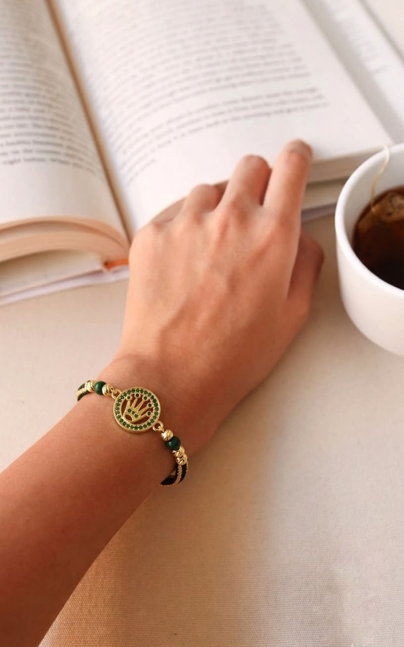 Pulsera artesanal con dije de medalla, corona grabada y detalles brillantes.